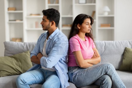 Photo for Displeased young indian couple sitting on couch, facing away from each other with arms crossed, showing tension and disagreement in their body language - Royalty Free Image