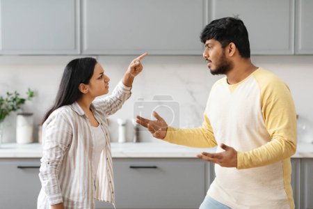 Photo for Furious millennial indian couple have fight, cozy modern kitchen interior. Angry young eastern woman shouting and gesturing while talking to her husband or boyfriend. Crisis in relationships, marriage - Royalty Free Image