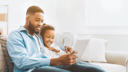 Photo for Father and daughter watching movie on tablet, spending time together at home - Royalty Free Image