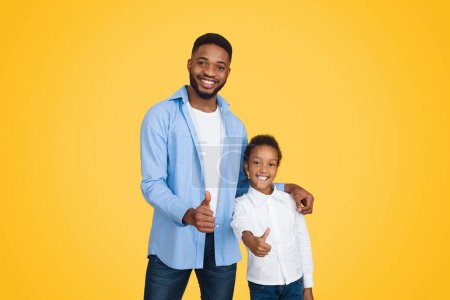 Foto de Recomendamos. Millennial afro padre y linda hija mostrando pulgares arriba, fondo naranja - Imagen libre de derechos