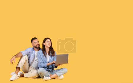 Relaxed man and woman sitting next to each other, using a laptop and looking away thoughtfully