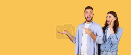 Man and woman in casual clothes acting surprised and pointing to empty space on yellow background