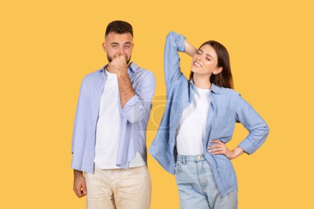 Téléchargez les photos : Un homme semble être dérangé par l'odeur, couvrant son nez, tandis qu'une femme à côté de lui s'étend joyeusement sur un fond clair - en image libre de droit