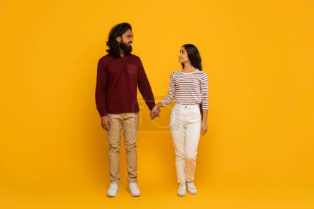 Foto de Un hombre y una mujer con atuendo casual se miran afectuosamente el uno al otro con un fondo amarillo - Imagen libre de derechos
