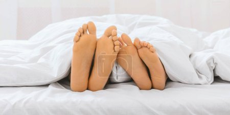 Foto de Una imagen cómoda e íntima de cuatro pies bajo un edredón blanco, retratando a una familia o grupo relajándose juntos - Imagen libre de derechos