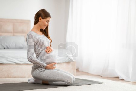 Foto de Una mujer embarazada tranquila en un estado pacífico practicando yoga prenatal en su dormitorio - Imagen libre de derechos