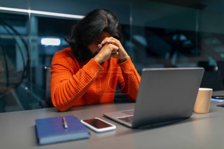 Un individuo abrumado con las manos apretadas sobre una computadora portátil, mostrando estrés, frustración o agotamiento en el trabajo