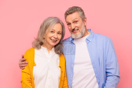 Téléchargez les photos : Homme et femme âgés joyeux dans le partage occasionnel une étreinte chaleureuse, illustrant la profondeur de leur relation durable et l'amour, debout et étreignant sur fond rose, plan studio - en image libre de droit
