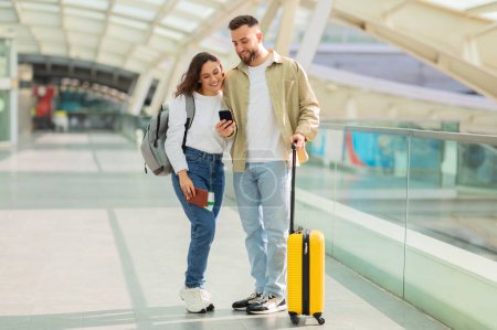 Photo for Smiling couple walking through a transportation hub with a smartphone, portraying connection and modern travel - Royalty Free Image
