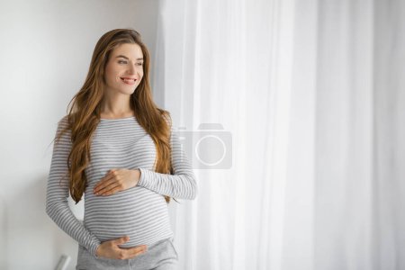 Foto de Joven embarazada en pose contemplativa mirando por la ventana con optimismo - Imagen libre de derechos