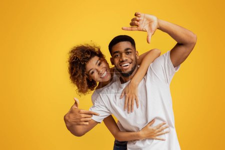 Téléchargez les photos : Noir millennial couple avoir amusant guy cadrage eux-mêmes avec mains sur orange fond panorama - en image libre de droit