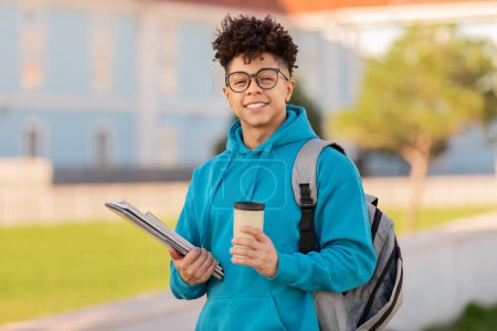 Photo for A content student brazilian guy stands outdoors holding textbooks and a coffee cup, with a backpack on, in front of a university - Royalty Free Image