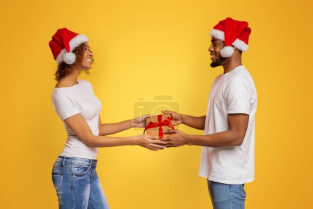 Photo for Family gift exchange. Black millennial couple giving present box to each other, orange studio background - Royalty Free Image