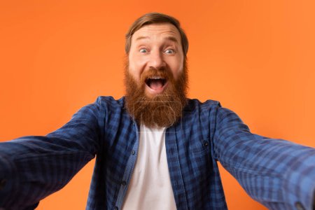 Photo for Excited Emotional Man With Red Hair And Beard Shouting Spreading Hands Looking At Camera, Posing For Selfie With Excitement, Reacting To Wow News Over Orange Studio Background, Selective Focus - Royalty Free Image