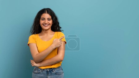 Femme confiante avec les bras croisés pointant vers le côté, regardant la caméra sur un fond bleu