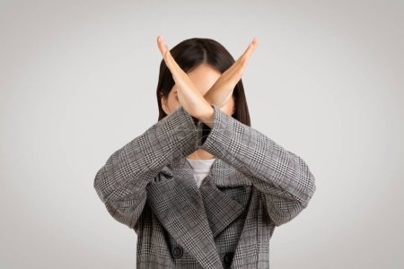 Photo for Businesswoman in houndstooth jacket making clear no gesture with her hands crossed in an X, signaling rejection, on gray background - Royalty Free Image