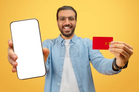 Foto de Hombre oriental sonriendo y mostrando un teléfono y tarjeta de crédito, adecuado para uso financiero o tecnológico - Imagen libre de derechos