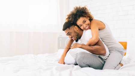 Happy loving young african american couple wearing pajamas bonding in bed, panorama with copy space