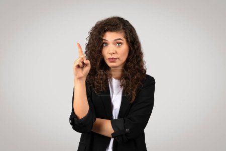 Photo for Woman in a suit with a raised finger, indicating caution or an important point - Royalty Free Image