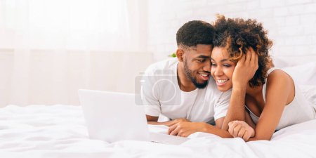 Foto de Una pareja afroamericana radiante disfrutando del tiempo junto con un portátil en un dormitorio lleno de luz, banner web - Imagen libre de derechos