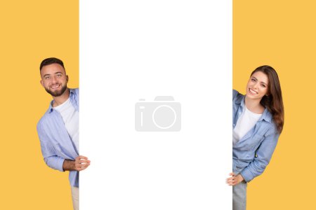 Téléchargez les photos : Homme et femme souriant et montrant une bannière blanche vierge sur fond jaune - en image libre de droit