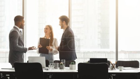 Téléchargez les photos : Trois collègues d'affaires discutent dans un environnement de bureau moderne et lumineux avec de grandes fenêtres en arrière-plan - en image libre de droit