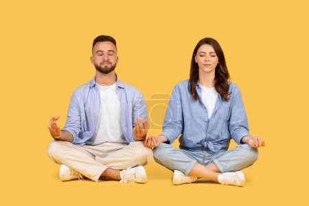 Foto de Hombre y mujer sentados con las piernas cruzadas y meditando en calma y serenidad sobre un fondo amarillo - Imagen libre de derechos