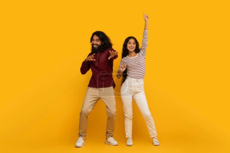 Téléchargez les photos : Couple heureux et énergique avec des vêtements tendance dansant joyeusement sur un fond jaune audacieux - en image libre de droit