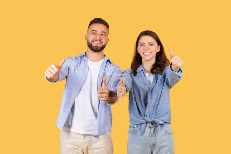 Foto de Dos adultos sonrientes, hombre y mujer, dando pulgares hacia arriba gestos sobre un fondo amarillo, expresando positividad y aprobación - Imagen libre de derechos