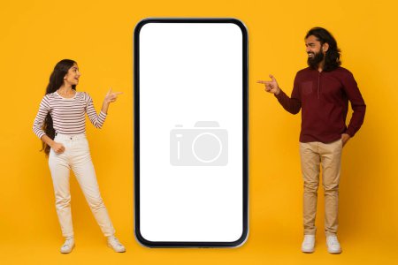 Foto de Hombre y mujer interactúan con una gran pantalla de teléfono inteligente en blanco sobre un fondo amarillo brillante - Imagen libre de derechos