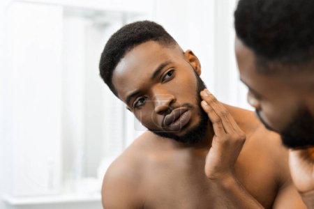 Capturando un momento de hombre afroamericano hidratando su piel, enfocado en el cuidado de la piel en un baño moderno