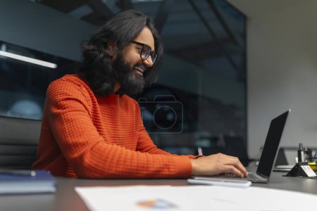 Téléchargez les photos : Heureux individu appréciant le travail sur son ordinateur à un bureau, montrant la satisfaction au travail - en image libre de droit