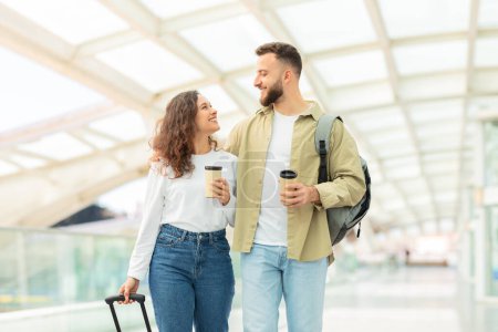 A man and woman enjoying their coffee while standing amidst the bustling ambiance of a modern transport hub