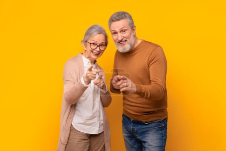 Téléchargez les photos : Concept de choix. Joyeux couple de personnes âgées en tenue décontractée pointant du doigt la caméra avec le sourire, posant ensemble en vous choisissant, debout sur fond jaune, plan studio - en image libre de droit