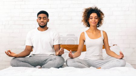 Téléchargez les photos : Un jeune couple afro-américain calme pratiquant la méditation ensemble dans un environnement serein de chambre - en image libre de droit