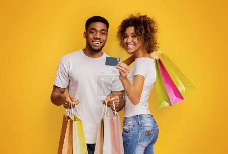 Foto de Joven pareja negra con bolsas de compras y tarjeta de crédito sobre fondo naranja estudio - Imagen libre de derechos
