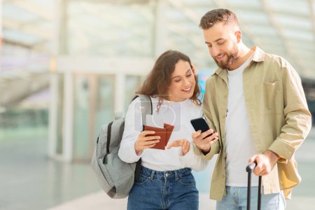 Téléchargez les photos : Un couple vérifie un smartphone en marchant dans un terminal, montrant l'intégration de la technologie et des voyages - en image libre de droit