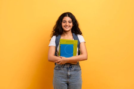 Photo for Confident student holding blue notebooks against a yellow background, symbolizing learning and education - Royalty Free Image