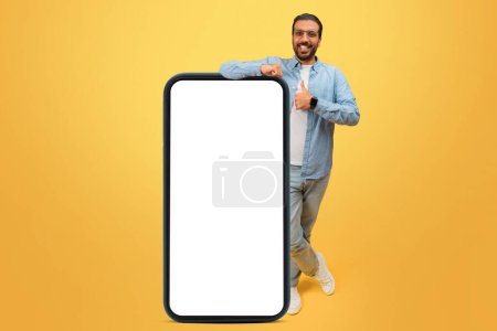 Foto de Hombre indio alegre dando un pulgar hacia arriba junto a un enorme teléfono inteligente con una pantalla en blanco para la publicidad - Imagen libre de derechos