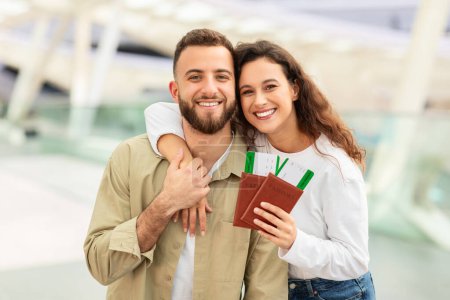 Photo for Close-up of a smiling couple holding passports, suggesting the excitement of travel, in front of a modern airport background - Royalty Free Image