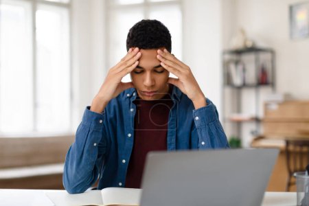 Téléchargez les photos : Adolescent noir concentré éprouvant des maux de tête tout en se concentrant sur ses études devant un ordinateur portable, concept de stress étudiant et de pression académique - en image libre de droit