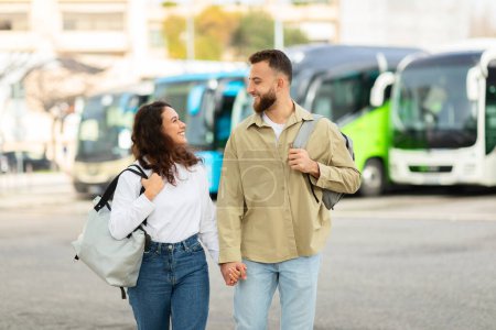 Foto de Una pareja feliz charlando y llevando mochilas en una estación de autobuses proporcionan un concepto de viaje y compañía - Imagen libre de derechos