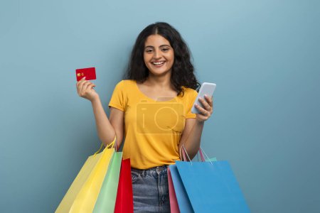 Téléchargez les photos : Une jeune femme joyeuse sourit en affichant une carte de crédit et un téléphone, représentant la facilité des transactions numériques - en image libre de droit