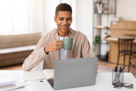Photo for Cheerful male teenager sips mug of coffee while engaging in an online learning session, exemplifying comfortable and enjoyable study environment - Royalty Free Image
