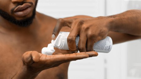 Hombre afroamericano aplicando una generosa cantidad de crema de afeitar en la mano antes del aseo, vista detallada