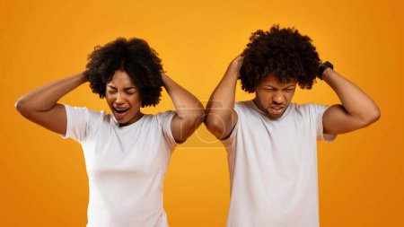 Photo for Devastated millennial african american man and woman wearing white t-shirts touching their heads and grimacing. Black couple experiencing difficulties, going through hard times, yellow background - Royalty Free Image