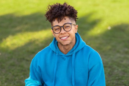 Retrato de cerca de un joven brasileño feliz con gafas con estilo y sonrisa natural sentado al aire libre