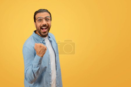 Photo for Eastern man with a beard and glasses looks astonished while pointing to himself against a yellow background - Royalty Free Image