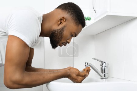Afrikanischer Mann reinigt seine Hände gründlich mit Seife und Wasser in einem sauberen, modernen Badezimmer
