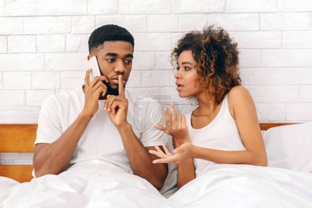 Foto de Mujer afroamericana hace gestos mientras discute con un hombre que está en una llamada telefónica, indicativo de tensión en la relación - Imagen libre de derechos